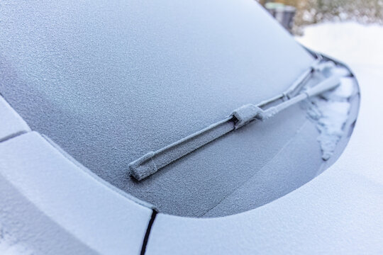 Windshield clearing priority centers on a frost covered wiper resting across opaque automotive glass, showing the practical need for ice removal before driving on a cold winter morning.