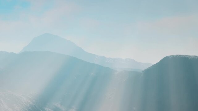 Light shines over distant mountains on a clear day. The scene shows layers of hills and a blue sky. It captures a natural landscape with no signs of human activity.