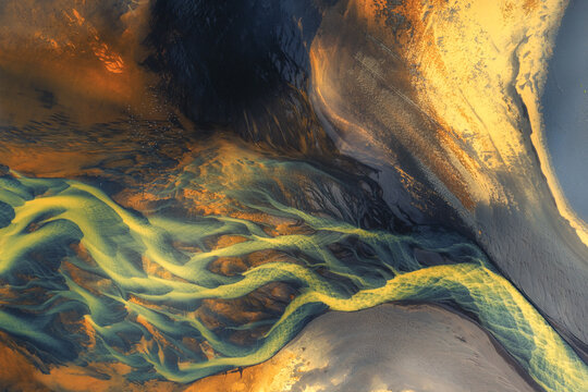 Aerial view of a vibrant braided river system in Iceland, featuring striking yellow sediment flowing through dark volcanic sand and silt deposits Iceland.