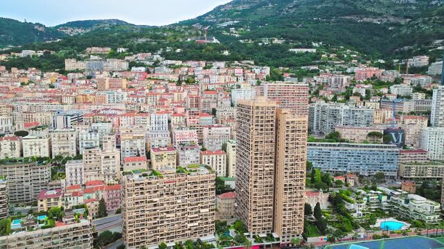 Drone view over the hillside cityscape of Monaco. Dense residential buildings, mountain slopes and urban streets create a scenic Mediterranean panorama.