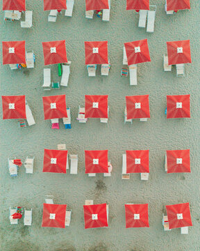 Aerial view of rows of red beach umbrellas and sun loungers arranged on the sandy beach in Cupra Marittima, Marche, Italy.