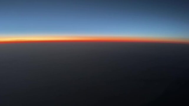 Pilot&rsquo;s point of view of a colorful sunrise over the North Atlantic Ocean from cruising altitude, with a glowing horizon and expansive cloud layers below.
