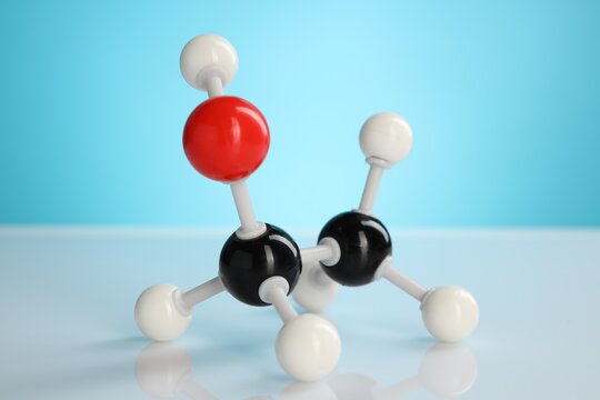 Chemical model of ethanol molecule on white table against light blue background, closeup