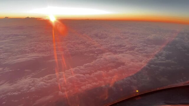 Pilot&rsquo;s point of view of a colorful sunrise over the North Atlantic Ocean from cruising altitude, with a glowing horizon and expansive cloud layers below.
