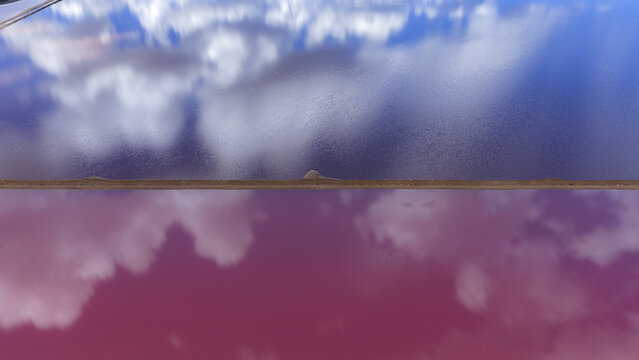 Aerial view of the industrial geometry of salt lake factories with vibrant pink and blue water separated by a narrow causeway reflecting the sky in Denham, Western Australia, Australia.