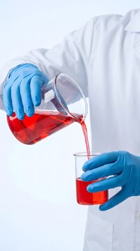 Scientist pouring red liquid from large beaker into smaller vessel.