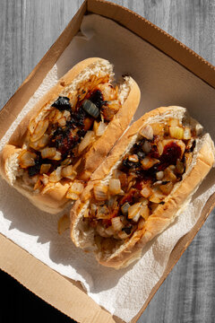 Hot dogs with fried onions in white finger bread rolls, made with pork sausages, in a cardboard takeaway tray background backdrop.