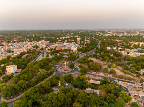 Aerial view of a roundabout with a central monument surrounded by lush green trees and urban buildings in Bikaner, Rajasthan, India.
