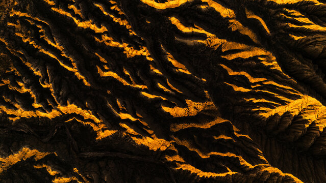 Aerial view of Ak-Say Valley with rugged mountain ridges illuminated by golden sunlight and deep shadows in At-Bashi District, Naryn Region, Kyrgyzstan.