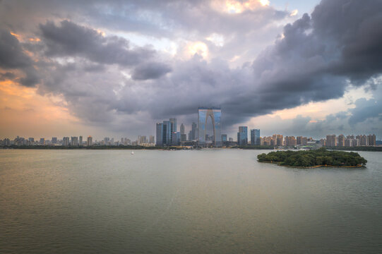 Aerial view of Jinji Lake with the Gate to the East skyscraper and modern city skyline under a dramatic cloudy sky in Suzhou, Jiangsu, China.