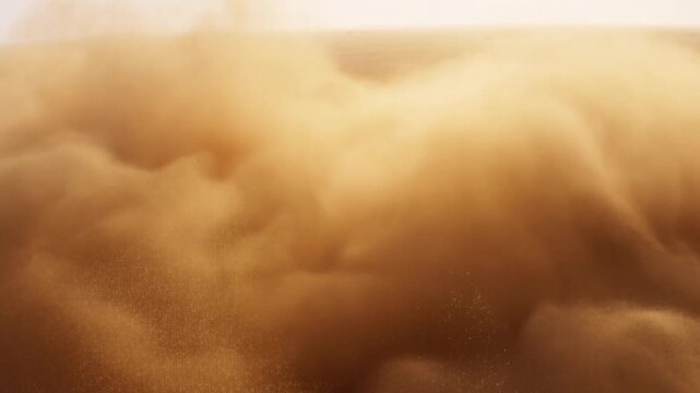 Aerial slow motion tracking pan of sand and dust clouds rolling and billowing across arid desert plain under warm golden light