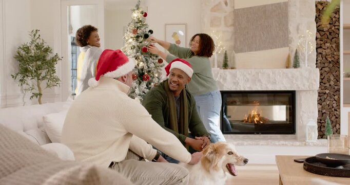 Diverse friends preparing for holiday, decorating Christmas tree, chatting and petting dog