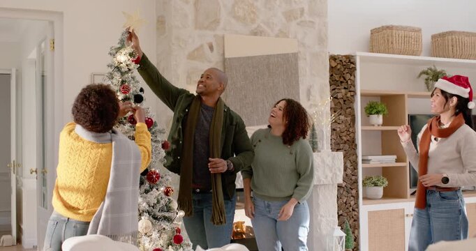 African American family handing star, man in green coat placing topper finishing tree home slipping
