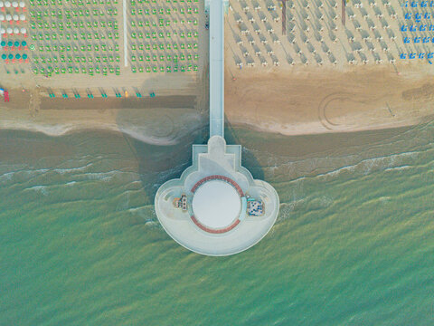 Aerial view of the Rotonda a Mare pier extending into the Adriatic Sea with rows of beach umbrellas on the sandy shore in Senigallia, Marche, Italy.