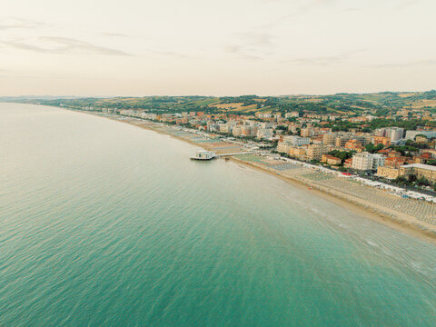 Aerial view of the Rotonda a Mare and the sandy coastline with rows of beach umbrellas and urban buildings along the Adriatic Sea in Senigallia, Marche, Italy.