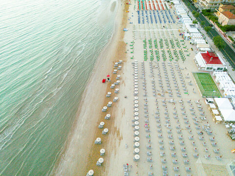 Aerial view of the sandy beach in Senigallia featuring rows of colorful umbrellas, calm Adriatic Sea waves, and coastal infrastructure in Senigallia, Marche, Italy.
