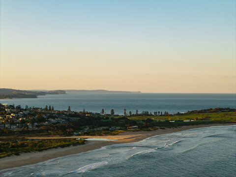 Aerial view of Dee Why Beach with its expansive coastline, residential area, and lush green parkland meeting the Pacific Ocean in Dee Why, New South Wales, Australia.