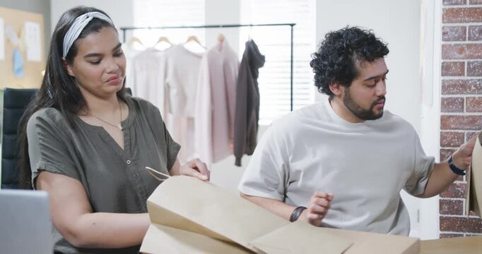 Diverse coworkers packing orders from laptop notifications, placing labeled boxes into paper bags