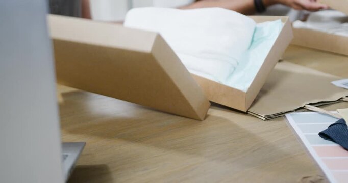 Hands are smoothing tissue and stacking kraft boxes after lid is being lifted for shipping