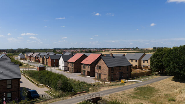 Aerial view of a modern residential housing development with brick houses, slate roofs, and paved streets surrounded by green fields in Radcliffe on Trent, England, United Kingdom.