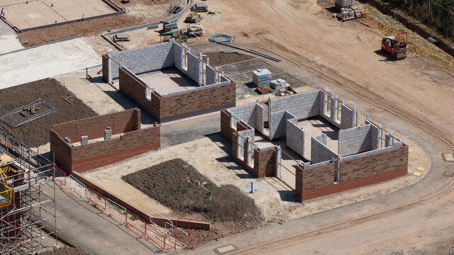 Aerial view of a residential construction site featuring partially built brick and block houses with exposed walls and dirt ground in Radcliffe on Trent, England, United Kingdom.