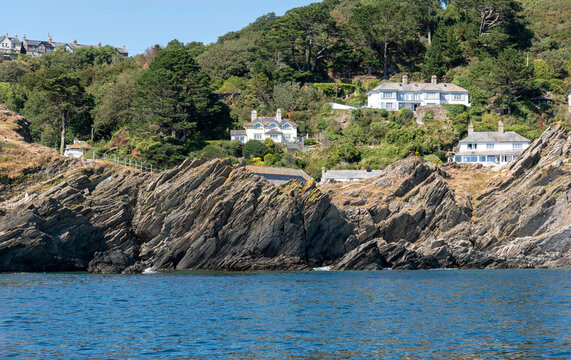 Polperro Cornwall England UK. 11.08.2026. White houses are built into a lush green hillside with dramatic rock formations leading down to the ocean in Polperro Cornwall England,