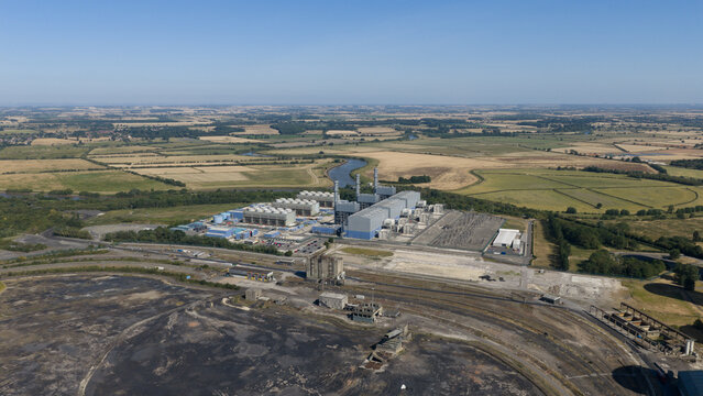 Aerial view of West Burton Power Station surrounded by industrial infrastructure, expansive agricultural fields, and a winding river in West Burton, England, United Kingdom.