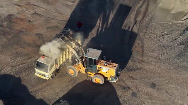 Heavy machinery loading gravel into a dump truck at a busy industrial construction site
