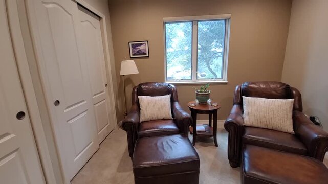 Narrow hallway seating nook with brown leather armchairs and small round table potted plant, windows