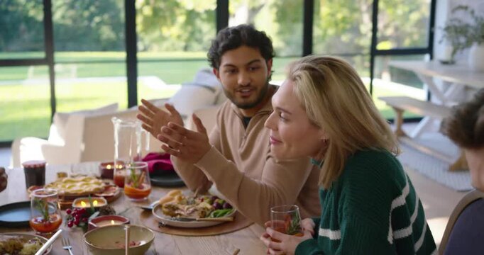 Diverse friends at wooden dining table, center man in tan sweater starting story