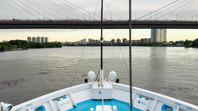 A white cruise ship sails smoothly under a large cable-stayed bridge. The calm river trip evokes a feeling of peaceful awe and wonder.