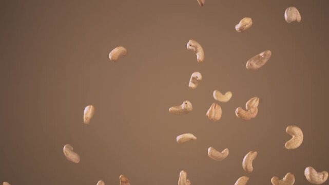 Cashew nuts flying through the air, isolated against a brown background.  Close up of raw cashew nuts falling and flying through the air with small pieces against a clean neutral background. Healthy. 