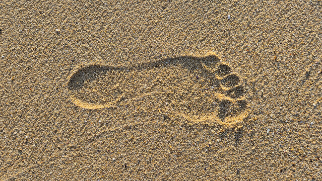 A single human footprint is clearly indented in the textured golden sand of a beach.