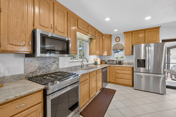 Warm wooden kitchen cabinets with stainless appliances, granite countertops sink faucet LED lighting