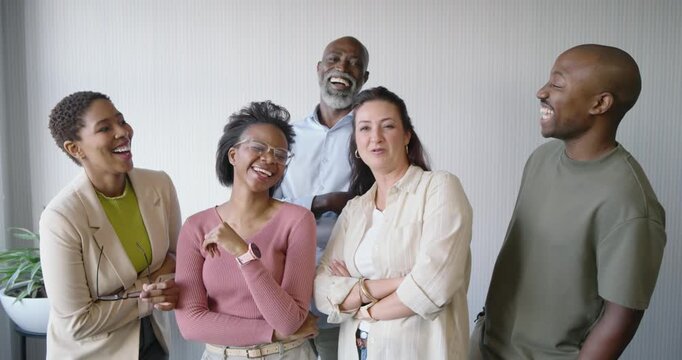 Diverse team reacting to left speaker gesturing, then laughing and facing camera by light wall