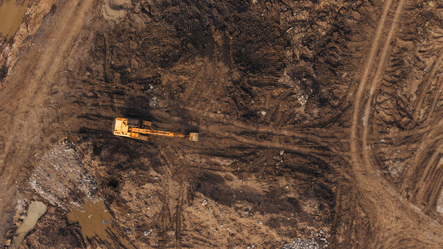 Aerial view of an excavator working on a muddy construction site with deep tire tracks and disturbed earth in India.
