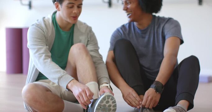 African American male friends sitting in studio tying shoes, phone between them, starting workout