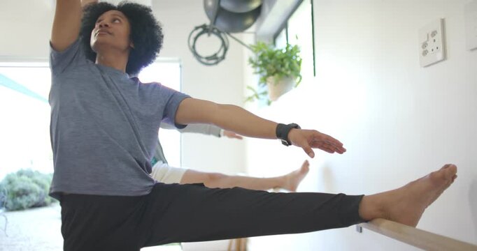 African American man and partner holding right leg on barre in studio, lifting arms for stretch