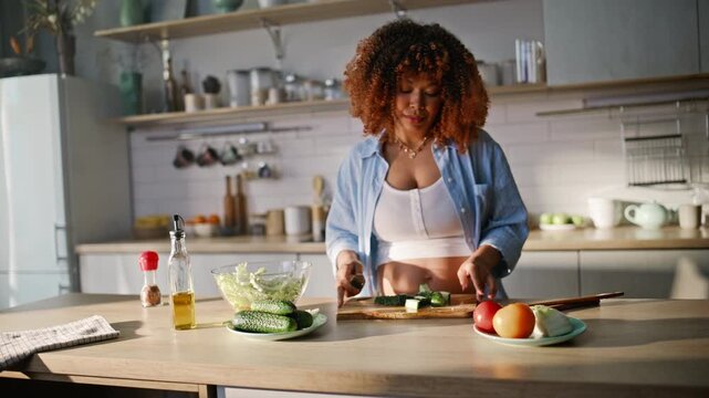 Expecting mom cutting cucumber home kitchen. Pregnant woman tossing salad bowl.
