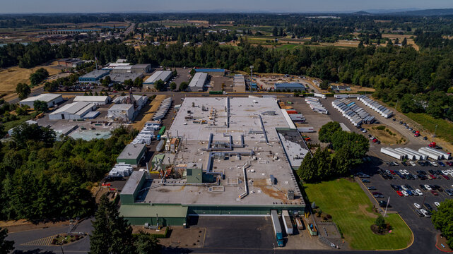 Aerial view of the battery factory facility with large industrial buildings, parking lots filled with cars, and rows of parked semi-trailers in Canby, Oregon, United States.