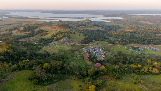 Aerial view of the Rally 2026 Paraguay event with tents and campsites in a rural landscape with forests and a river in the background in Nueva Alborada, Itapua Department, Paraguay.