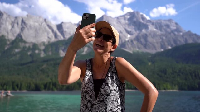 Woman influencer on the phone with german Zugspitze alps and Eibsee lake view in the background