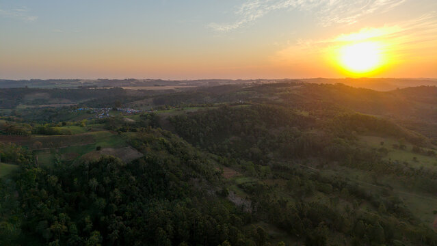 Aerial view of the rolling hills and lush forests of Nueva Alborada at sunset, with golden light illuminating the landscape in Nueva Alborada, Itapua Department, Paraguay.