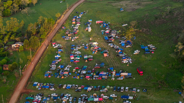 Aerial view of Rally Paraguay 2026 campsite with numerous tents and parked vehicles arranged in a grassy field near a dirt road in Nueva Alborada, Itapua Department, Paraguay.