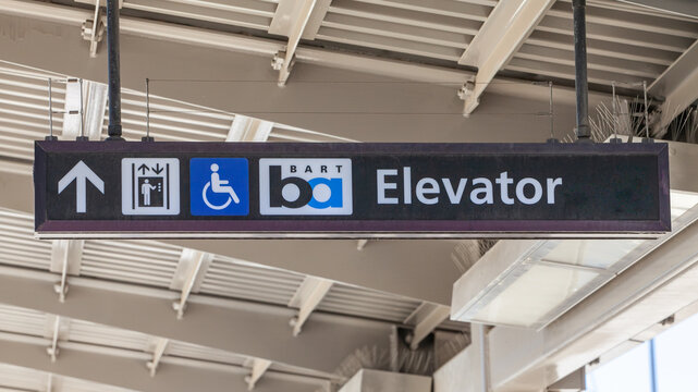 BART station wayfinding sign showing elevator direction with accessibility symbol and transit logo in indoor facility