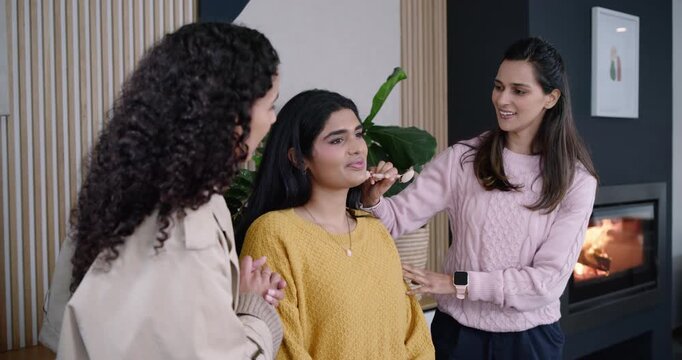 Diverse women filming makeup in studio, stylist dabbing sponge on model, showing bottle to camera
