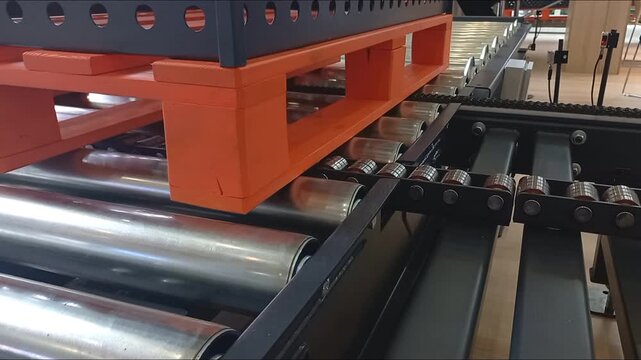 Close up view of bright orange plastic pallet on automated industrial metal roller conveyor line at warehouse distribution center presenting modern sorting logistics shipping technology concept