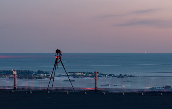 Aerial view of a camera on a tripod on the roof of Kalasatama skyscraper overlooking the coastline and sea at dusk in Helsinki, Uusimaa, Finland.