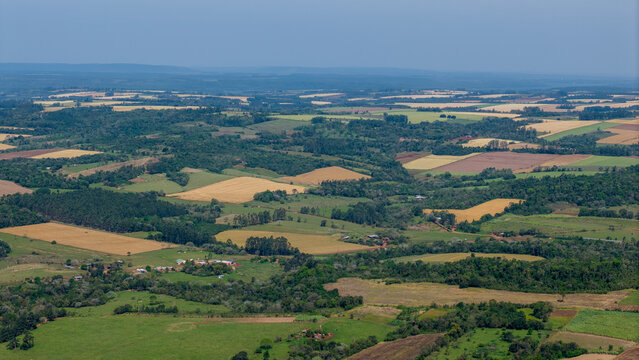 Aerial view of the rural landscape featuring patchwork agricultural fields, patches of dense forest, and scattered farmhouses under a clear sky in Nueva Alborada, Itapua Department, Paraguay.
