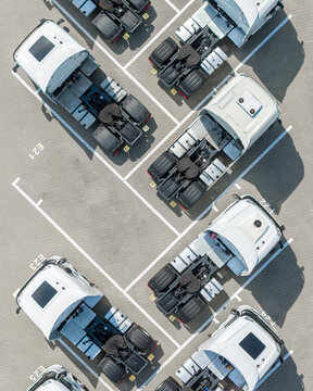 Aerial view of white semi-trucks parked in an orderly parking lot with marked spaces in Poland.